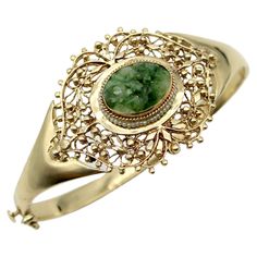 This elegant bracelet is made of 14k gold and decorated with a central reticulated piece of green jade. The center jade piece protrudes about a 1/4 of an inch from the gold setting and is carved with flower patterns. A lovely ring of seed pearls decorates the gold setting around the oval jade stone. From the central jade, as if emitting sinuous line-work, the gold work has a woven lace-like gold organic pattern detailed with beads of gold. The central piece was once a brooch and has been seamles Modern Bracelets, Organic Pattern, Gold Work, Elegant Bracelet, Lovely Ring, Seed Pearl, Jade Stone, Statement Bracelet, Green Jade