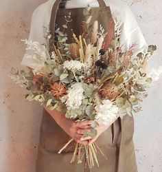 a person wearing an apron holding a bouquet of flowers and greenery in their hands