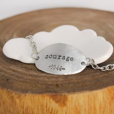 It only takes one little word to touch someone’s heart.This inspirational word bracelet makes a memorable gift idea that your recipient is sure to cherish. Artistically designed to perfection, it features a large oval shaped pendant stamped with the word “courage” and a whimsical leaf motif. Suspended from coordinating chain, it features a delicately hand hammered edge that adds layers of character. When worn, it caresses the top of your wrist beautifully and is sure to become a treasured access Meaningful Sterling Silver Bracelets, Meaningful Adjustable Charm Bracelet, Meaningful Faith-inspired Bracelet Jewelry, Meaningful Sterling Silver Friendship Bracelets, Inspirational Stamped Jewelry For Best Friend Gift, Inspirational Hand Stamped Bracelet Jewelry, Inspirational Hand Stamped Jewelry Bracelet, Inspirational Engraved Bracelets For Everyday, Inspirational Engraved Everyday Bracelets