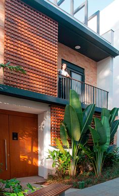 a person standing on the balcony of a house with plants and trees in front of it