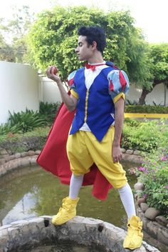 a man dressed up like snow white standing in front of a pond with his hand on his hip