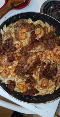 a pan filled with shrimp and pasta on top of a stove next to a spatula