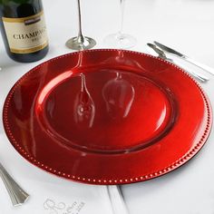 a red plate sitting on top of a white table next to a bottle of wine