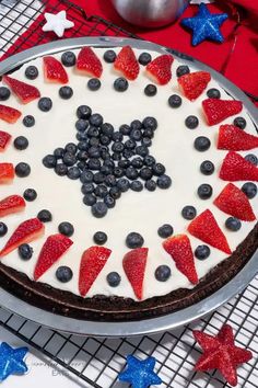 a cake decorated with blueberries, strawberries and red white and blue stars on a cooling rack