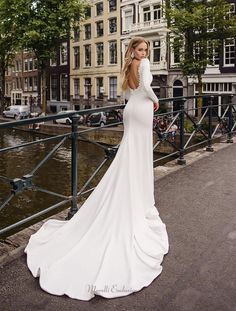 a woman in a white wedding dress is standing on a bridge near some buildings and trees