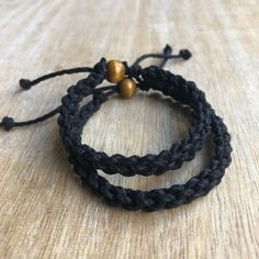 two black braided bracelets with gold beads on a wooden surface, close up