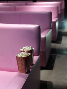 some pink seats with popcorn in them and one bag sitting on the seat next to it