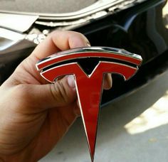 a hand holding a red and black tesla emblem