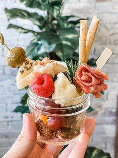 a person holding up a small jar filled with fruit and crackers on top of it