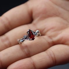 a person is holding a ring with a red stone in it's middle finger