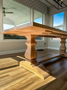 a large wooden table in an empty room with wood flooring and big windows looking out onto the ocean