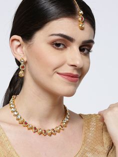 This handcrafted jewelry set consists of a necklace, a maang tikka and a pair of matching drop earrings. The necklace has a maroon color-theme with green accents, comes with kundan stone studs, is gold-plated, and secured with an adjustable drawstring closure. A matching maang tikka comes with kundan stone studs, is gold-plated, and can be secured with a hook closure. A pair of matching drop earrings come with kundan stone studs, are gold-plated, and are secured with a post and back closure. The Chandbali Jewelry Sets For Puja, Dual-tone Chandbali Jewelry For Puja, Festive Dual-tone Temple Jewelry Sets, Festive Gold Plated Tikka As A Gift, Festive Temple Jewelry Tikka With Jeweled Details, Dual-tone Gold Plated Jewelry, Dual-tone Kundan Temple Jewelry Sets, Festive Dual-tone Chandbali Jewelry Sets, Luxury Jeweled Bridal Necklace In Temple Jewelry Style