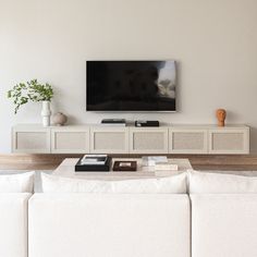 a living room with white couches and a flat screen tv mounted on the wall