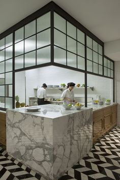 two people in a kitchen preparing food on top of marble counter tops and black and white checkered flooring