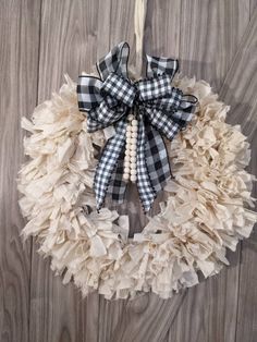 a white and black wreath hanging on a wooden wall with burlocked ribbon