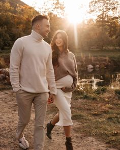 a man and woman walking down a path holding hands while the sun is setting behind them