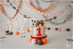 a sports themed birthday cake with balls and garlands around it on a white table