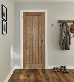 a wooden door in a white room with shoes hanging on the wall and coat rack