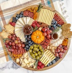 a platter filled with different types of cheeses and fruit on top of a checkered table cloth