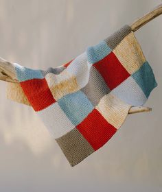 a multicolored knitted blanket hanging from a tree branch in front of a white wall