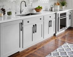 a kitchen with white cabinets and wooden floors is pictured in this image, there are fruit on the counter