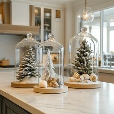 two glass domes with christmas trees under them on a counter top in front of a window