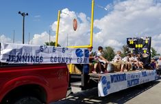 a group of people riding on the back of a red truck with an american football banner