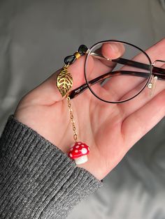 Beautiful mushroom glasses charm: red and white glass mushroom bead on gold-tone chain, with matching metal gold leaf charm.  Single piece made to add to one arm of your glasses.  Silicone loop allows it to easily be added and removed from your glasses to instantly upgrade any outfit! Also available as a full chain: https://www.etsy.com/listing/1370319289/ Approximate chain length: 2 inches. Eye Glasses Accessories, Cute Glasses Accessories, Glasses Accessories Jewelry, Beads Glasses, Mushroom Accessories Aesthetic, Fairy Glasses, Chain For Glasses, Diy Chain Accessories, Glasses Jewelry