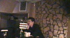 a man sitting at a table in front of a rock wall with an electronic keyboard