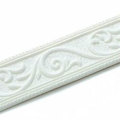 a white decorative piece with an ornate design on the top and bottom, is shown in front of a white background