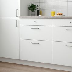 a kitchen with white cabinets and counter tops next to a potted plant on the counter