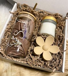 an open box with two jars and a flower on the inside, sitting on a furry surface