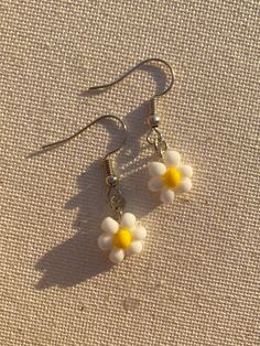 two white and yellow flowers are hanging from silver earwires on a beige surface