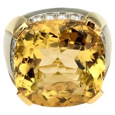 This large and luxurious modern ring is a one-of-a-kind piece from a high jewelry collection, demonstrating exceptional craftsmanship. It features a 19x19mm cushion-cut citrine set in an 18kt dual-tone gold band. The citrine is mounted atop a white gold band with a satin finish, complemented by yellow gold highlights in a high polish finish, creating a striking contrast. Instead of a traditional halo, the diamonds are elegantly placed below the girdle of the citrine, enhancing the ring's unique Luxury Dual-tone Jewelry, Luxury Dual-tone Traditional Jewelry, Luxury Square Cut Diamond Ring In Yellow Gold, Luxury Yellow Gold Square Cut Diamond Ring, Cushion Cut Gemstones For Formal Fine Jewelry, Cushion Cut Fine Jewelry Gemstones For Formal Occasions, Luxury White Gold Citrine Ring, Luxury Gemstones With Diamond Accents, Luxury Diamond Topaz Ring With Cushion Cut