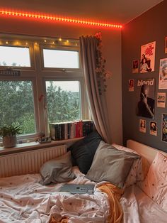 an unmade bed in front of a window with posters on the wall