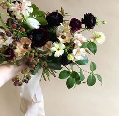 a bouquet of flowers is being held by someone's hand with a white ribbon