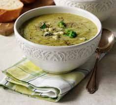 two white bowls filled with broccoli soup on top of a table next to bread