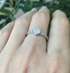 a woman's hand with a diamond ring on her finger and green plant in the background