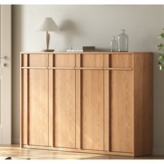 a wooden cabinet sitting next to a lamp on top of a hard wood floor in front of a white wall