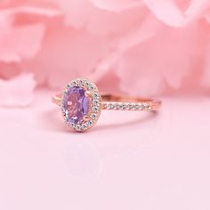 an oval shaped pink sapphire and diamond ring on a pink background with flowers in the foreground