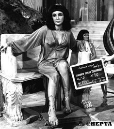 a woman sitting on top of a wooden bench next to another woman holding a sign