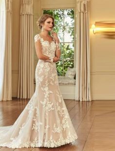 a woman in a wedding dress standing on a hard wood floor next to a window