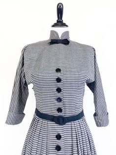 "A fabulously chic vintage day dress from the early 1950s! Medium weight cotton blend in horizontal black, white and gray stripes. Fitted waist and bloused bustline with cuffed ¾ length sleeves cut in one with the bodice. High Nehru collar accented with tailored grosgrain ribbon bow. A-line skirt with gathers at each hip, front and back. Dress closes up the front with a row of 22 buttons that extend from bust to hem. Small shoulder pads and short metal zipper at back neck. Unlined, missing origi Vintage Striped Dresses For Work, Vintage Striped Dress For Work, 1950s Vintage Dress With Buttons, Vintage Striped Workwear Dresses, Retro A-line Dress With Button Closure, Classic A-line Vintage Dress With Button Closure, 1950s Vintage Dress With Buttons For Daywear, 1950s Vintage Dress With Button Closure, Grosgrain Ribbon Bows