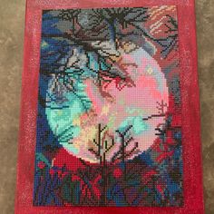 a cross - stitch picture with trees and the moon in the background on a red mat