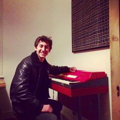 a man sitting at a red piano with his hands on the keyboard and smiling for the camera