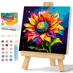 an easel with paint and brushes on it next to a colorful flower painting kit