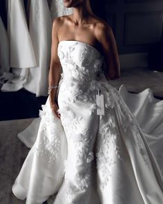 a woman in a white dress standing next to some dresses