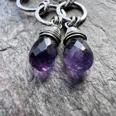 Two genuine amethyst teardrops have been wrapped in sterling silver wire. The natural stones hang from a set of sterling silver circles which I have formed, soldered, and hammered by hand. The earrings dangle from handmade sterling silver earwires. The silver has been oxidized and polished to create an antique patina finish. Be sure to see all photos and video for size and color reference. Amethyst Size: About 5x8mmTotal Earring Length (Including Earwire): Just under 2.25"Earring Weight: About 1 Nickel Free Briolette Teardrop Earrings In Sterling Silver, Nickel-free Briolette Teardrop Sterling Silver Earrings, Sterling Silver Briolette Teardrop Gemstone Earrings, Purple Sterling Silver Teardrop Dangle Earrings, Silver Amethyst Wire Wrapped Earrings, Wire Wrapped Amethyst Drop Earrings, Teardrop Amethyst For Jewelry Making, Handmade Amethyst Teardrop Earrings, Purple Wire Wrapped Drop Earrings