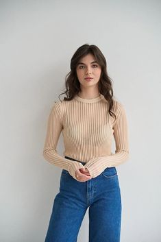 a woman standing in front of a white wall with her hands on her hips and looking at the camera