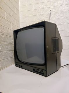 an old black television sitting on top of a white table next to a brick wall